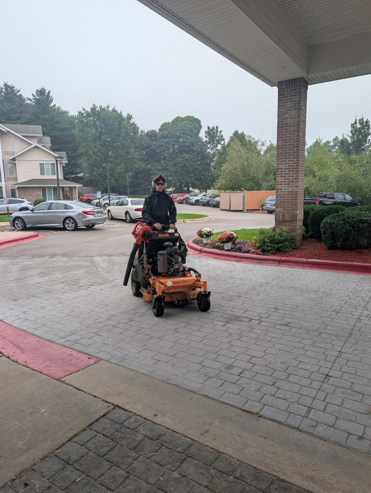 Crew member clearing a paved drive with a stand-on blower