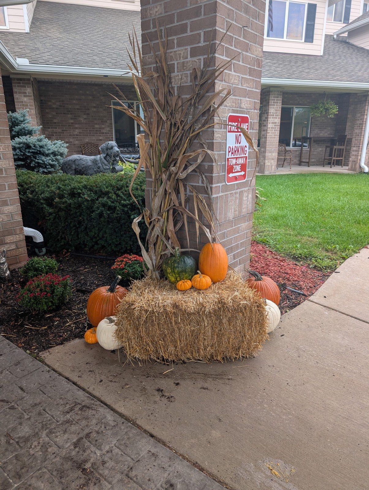 Straw bale, corn stalk, and pumpkin display at the base of a brick pillar