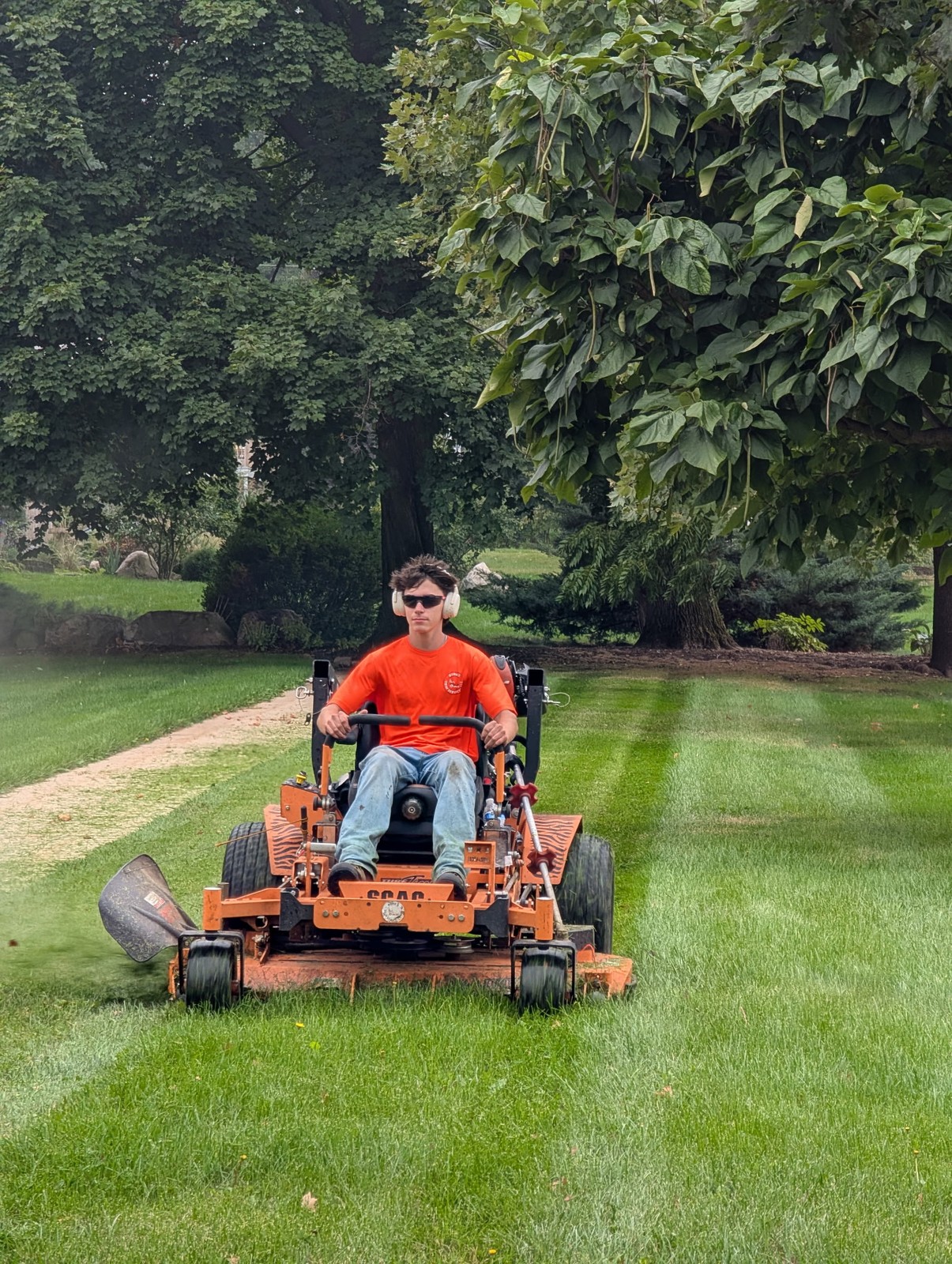 Crew member on a stand-on mower with bright stripes behind the mower