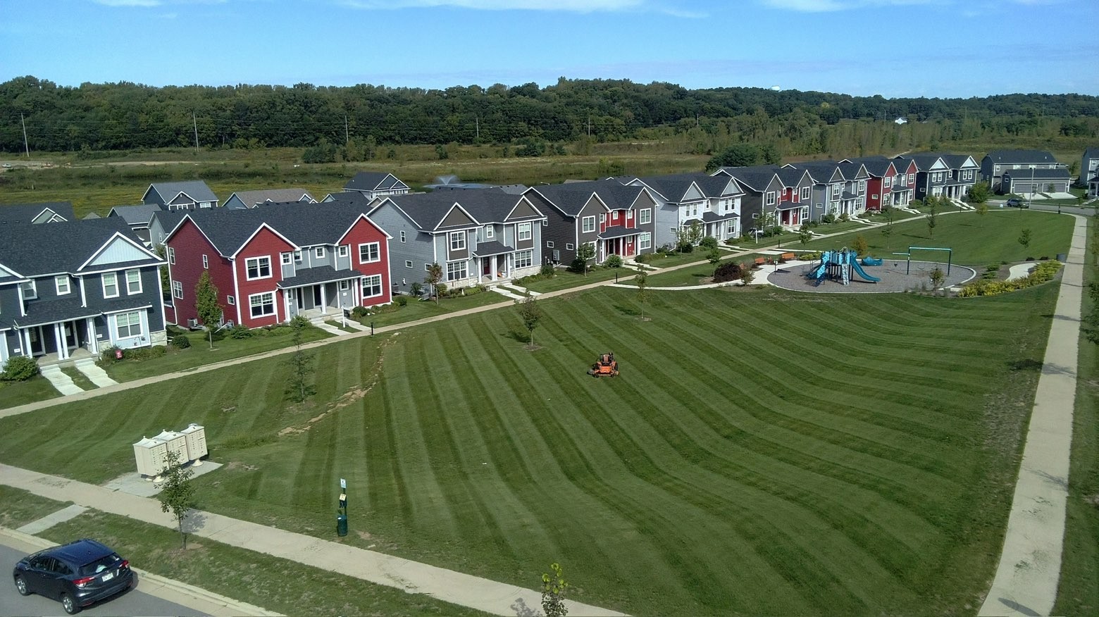 Aerial view of a mower striping a large common lawn in front of a row of townhomes