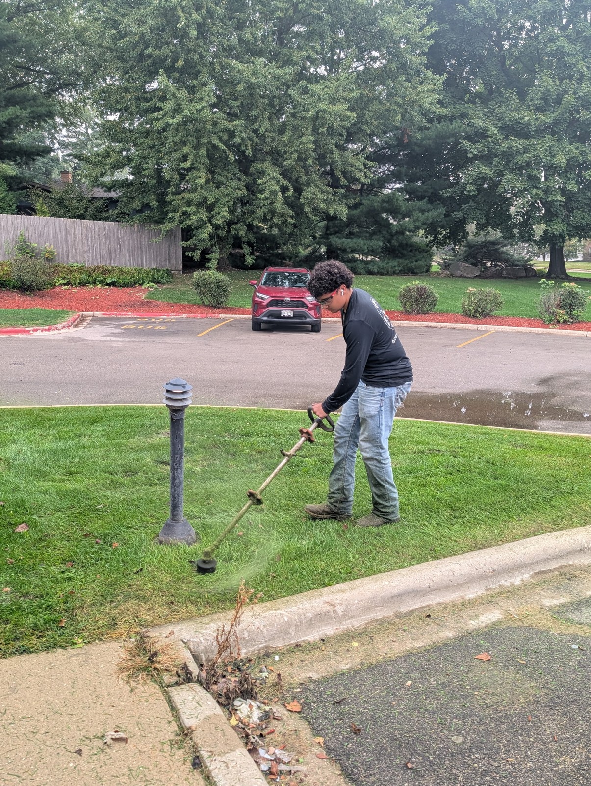 Crew member string trimming along a parking lot curb